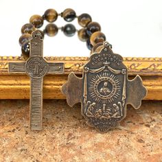 This stunning single decade features golden-brown tiger eye gemstones and solid bronze pieces cast from antiques using the lost wax method. The front of the 2" cross features St. Michael in battle. The reverse side depicts angels kneeling in adoration before the Holy Eucharist in the monstrance. This cross pairs nicely with the handsome St. Benedict Crucifix which also measures 2” in length. A perfect gift for anyone with a devotion to St. Michael, St. Benedict, or for Confirmation, or a priest. Brown Crucifix Spiritual Jewelry, Antique Bronze Crucifix Jewelry, Spiritual Brown Crucifix Jewelry, Brown Spiritual Crucifix Jewelry, Holy Eucharist, Brown Tiger, Decade Rosary, Brown Tiger Eye, St Benedict