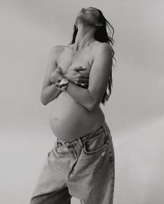 a pregnant woman standing with her hands on her stomach and looking up into the sky