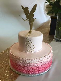 a white and pink cake with a gold tinker fairy on top sitting on a table