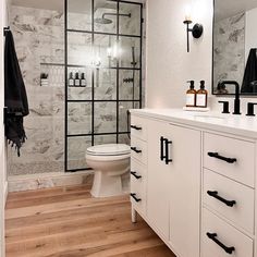 a bathroom with white cabinets and black handles on the vanity, along with a glass shower door