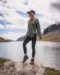 a woman standing on top of a rock next to a body of water