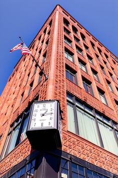 a large brick building with a clock on the side and an american flag hanging from it