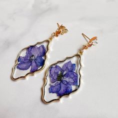 Treat yourself with our Purple Pressed Flower Resin Earrings, blending nature's beauty with contemporary elegance. Each earring features real pressed purple flowers and glitter encased in resin, creating a unique piece of minimalist jewelry. Perfect for nature lovers, these earrings add a touch of floral charm to any outfit, embodying femininity and grace effortlessly. Elegant Resin Earrings With Flower Charm, Elegant Resin Flower Earrings, Elegant Resin Flower-shaped Earrings, Elegant Resin Earrings With Pressed Flowers, Elegant Pressed Flower Resin Earrings, Elegant Resin Birth Flower Earrings, Elegant Clear Resin Earrings, Elegant Silver Earrings With Pressed Flowers, Purple Pressed Flower Drop Earrings