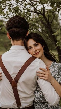 a man and woman embracing each other in front of some trees with their backs to the camera