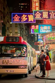 a man and woman standing in front of a bus on a city street at night