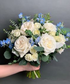 a bouquet of white and blue flowers being held by someone's hand on a gray background