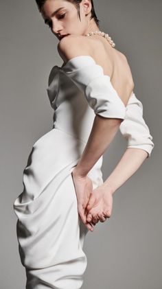 a woman in a white dress with her hands on the back of her body, posing