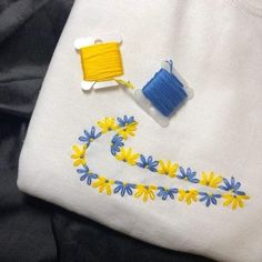 two spools of thread sitting on top of a white t - shirt with yellow and blue flowers