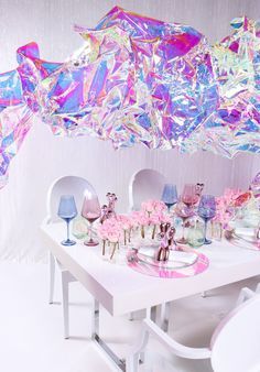 a white table topped with lots of pink and purple flowers next to a chandelier