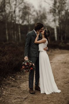 a bride and groom kissing in the middle of a dirt road with trees behind them