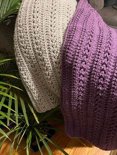 two crocheted hats sitting on top of a wooden floor next to a plant