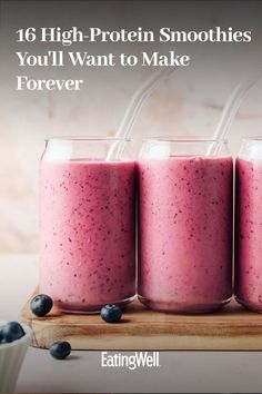 three glasses filled with blueberries on top of a wooden table next to some berries