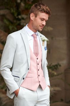 a man in a pink suit and white shirt is looking down at his pocket while wearing a boutonniere