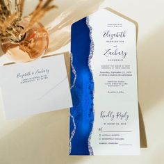 an elegant blue and white wedding suite is displayed on a table next to a vase with dried flowers