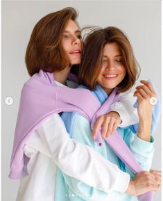 two women are hugging each other while wearing sweaters and scarves on their shoulders