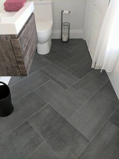 a bathroom with grey tile flooring and white walls, along with a black trash can