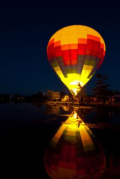 a colorful hot air balloon is lit up at night with its reflection in the water