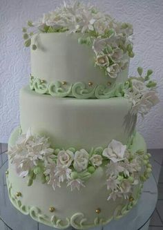 a three tiered cake with white flowers and green icing on a glass table