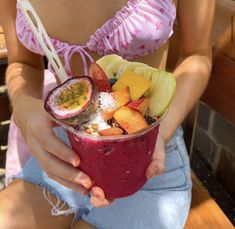 a woman is holding a fruit smoothie in her hands