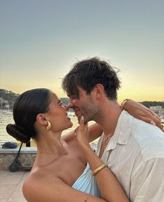 a man and woman standing next to each other in front of a body of water