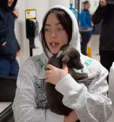 a woman holding a puppy in her arms while wearing a hoodie and looking at the camera