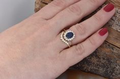 a woman's hand wearing a gold ring with an oval blue stone surrounded by smaller white stones