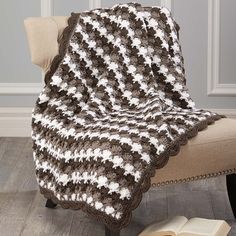 a crocheted afghan sits on a chair with an open book