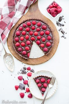 a chocolate raspberry pie on a wooden cutting board with two bowls of raspberries in the background