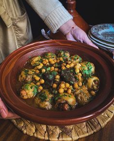 a person holding a plate full of food on top of a wooden table next to plates