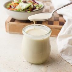 a spoon pouring milk into a glass jar next to a bowl of salad on a cutting board