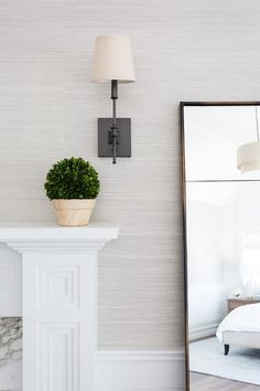 a white room with a mirror, lamp and potted plant