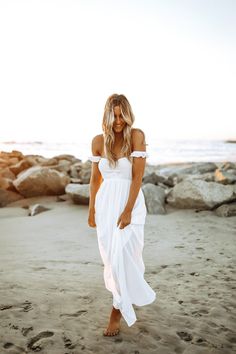 a woman standing on top of a sandy beach next to the ocean wearing a white dress