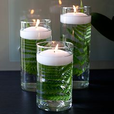 three candles are sitting in glass vases with green leaves on the inside and outside