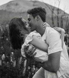 a man and woman kissing each other in front of flowers with mountains in the background