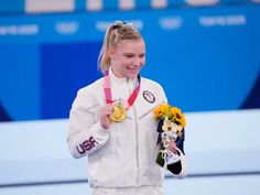 a woman is holding up her gold medal and flowers while standing on the podium in front of an audience