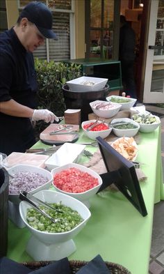 a man preparing food on top of a green table covered in bowls and pans