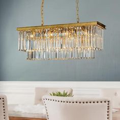 a chandelier hanging over a dining room table with white chairs and a potted plant