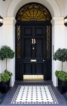 an image of a black front door with potted plants on either side and the letter b in gold