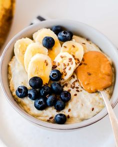 a bowl of oatmeal with bananas and blueberries on top, next to a spoon