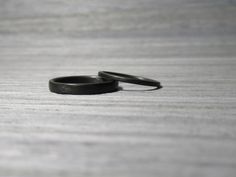 two black wedding rings sitting on top of a wooden table next to each other,