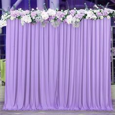 purple drapes with white flowers and greenery on the top are set up for a wedding ceremony