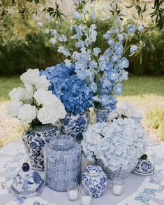 blue and white flowers are in vases on a table with other items around it