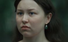 a close up of a person with blue eyes wearing earrings and looking at the camera