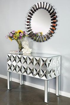 a mirror on the wall next to a table with flowers and vase in front of it