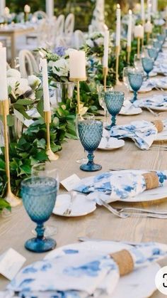 a long table is set with blue and white dishes, candles, and greenery