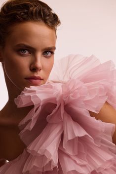 a woman wearing a pink dress with ruffles around her neck and shoulders, posing for the camera