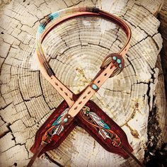 a pair of leather scissors sitting on top of a piece of tree trunk with feathers painted on it