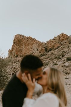 a man and woman kissing in front of a rocky mountain side with desert vegetation behind them