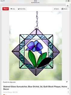 a stained glass sun catcher with blue flowers hanging from it's center and green leaves in the middle