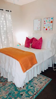 a white bed with orange and red pillows on it in a bedroom next to a window